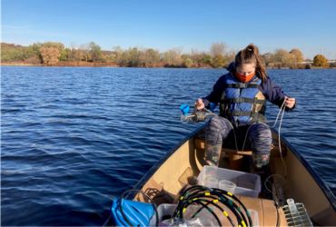 University of Akron student collects water samples from a lake while conducting field research in a small boat.